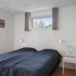 Schlafzimmer mit Bett, Fenster und Stuhl. Wände weiß verkleidet, Decke mit Paneelen.