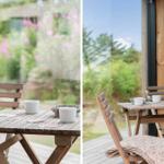 Holztisch mit zwei Stühlen und Tassen auf Terrasse mit Blick auf Garten.