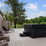 Terrasse mit Whirlpool, Liegestühlen und Beistühlen. Hintergrund: Wald und blauer Himmel.