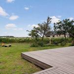 Holzterrasse mit Blick auf Grasland, Bäume und Ferienhaus im Hintergrund.