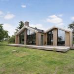 Moderne Holzhütte mit großem Terrassenbereich und Glasfassade im Grünen.