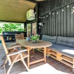 Terrasse mit Holztisch, Stühlen und Sofa aus Paletten. Hintergrund: Grillbereich und Wald.