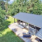 Holzterrasse mit Liegen und Grill, umgeben von grünem Rasen und Bäumen.