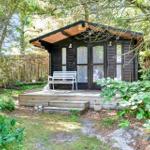 Holzhütte mit Terrasse und weißem Stuhl im Wald. Fenster mit weißen Vorhängen.