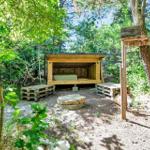 Holzkonstruktion mit Bett im Wald, umgeben von Bäumen und Pflanzen.