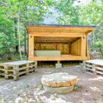 Holzkonstruktion mit Bett im Freien, umgeben von Bäumen und Paletten.