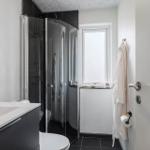 Badezimmer mit Dusche, Toilette und Waschtisch. Weiße Wände und schwarze Fliesen.