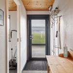 Eingangsbereich mit Holzdecke, Tür mit getöntem Glas und Holzbank mit Flasche.