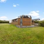 Holzhaus mit Terrasse und Garten. Himmel blau, Gras grün.