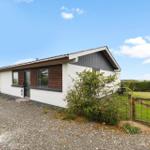 Moderne Ferienhaus mit weißen Wänden und braunen Holzverkleidungen, umgeben von Grünfläche und Zaun.