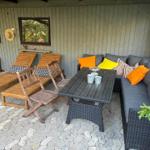 Terrace with seating group, table, and lounge chairs. Wooden and wicker furniture on stone paving.