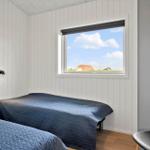 Zwei Betten mit blauen Bettdecken, Fenster mit Blick auf Haus und Himmel, Holzboden, Wandlampe und Stuhl.