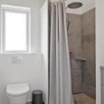 Badezimmer mit Dusche, Toilette und Waschbecken. Fenster sorgt für Tageslicht.
