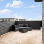 Terrasse mit Sitzgruppe und Holzboden. Schwarze Holzwand und Blick auf Ferienhäuser.