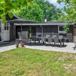 Haus mit Terrasse, Tisch, Stühlen und Sonnenschirm. Grasfläche und Bäume im Hintergrund.