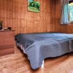 Schlafzimmer mit Holzwand, Bett, Schrank und Fenster mit Blick auf Wald.