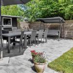 Terrasse mit Tisch, Stühlen, Sonnenschirm und Schaukel unter Bäumen.