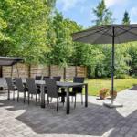 Garten mit Tisch, Stühlen, Sonnenschirm und Schaukel unter Bäumen.