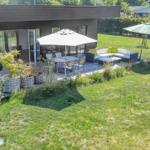Terrace with seating area, table, and umbrella. Lawn and plants surround the terrace.