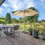 Deck with table, chairs, and umbrellas. Green fields and trees in the background.
