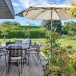 Deck with table, chairs, and umbrella. Lawn and hedges in the background.