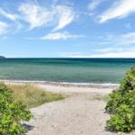 Sandy path leads to the beach with clear sea and blue sky.