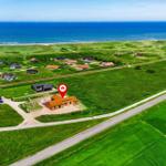 Haus mit rotem Dach liegt in grüner Landschaft neben Strand und Windkraftanlagen.