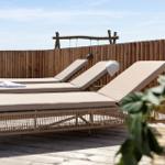 Drei Liegestühle auf einer Holzterrasse mit Holzgeländer und Pflanze im Vordergrund.