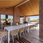 Terrasse mit Esstisch, Sitzgelegenheiten und Kamin. Holzdecke und Ziegelmauer.
