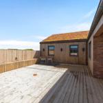 Terrasse mit Holzdecke, Sitzgelegenheit und Gartenzaun. Hintergrund: Holzhaus mit grüner Dachdeckung.