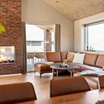 Wohnzimmer mit braunem Sofa, Kamin und großem Fenster. Holzboden und hölzerner Tisch.