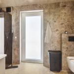 Badezimmer mit Dusche, Toilette und Fenster. Wände und Boden sind aus Stein.