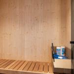 Sauna mit Holzwand, Sitzbank, Eimer und Reinigungsmittel.