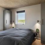 Schlafzimmer mit Bett, zwei Fenstern und zwei Schränken. Decke aus Holzlamellen.