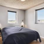 Schlafzimmer mit Bett, zwei Fenstern und Holzboden. Decke aus Holzdielen.