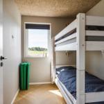 Zimmer mit Doppelstockbett, Fenster und Holzboden.
