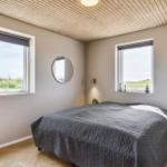 Schlafzimmer mit Doppelbett, zwei Fenstern und runden Spiegel an den Wänden.