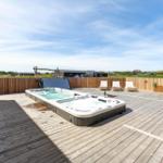 Terrasse mit Whirlpool und Liegen, umgeben von Holzzaun und Grünland.