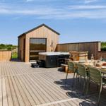 Terrasse mit Hot Tub, Esstisch und Holzhaus im Hintergrund.