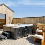 Außenbereich mit Whirlpool, Holzbad und Holzterrasse. Hintergrund: Holzhaus mit Glasfront.