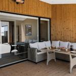 Terrasse mit Sitzgruppe und Tisch. Holzwände und Glasfront. Im Hintergrund Blick in das Haus.