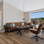 Wohnzimmer mit braunem Sofa, zwei Sesseln und Blick auf Terrasse.