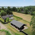 Modernes Haus mit Terrasse, umgeben von Grün und einem See im Hintergrund.
