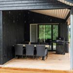 Terrasse mit Tisch, Stühlen und Grill unter schwarzem Dach. Regen fällt.
