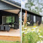 Terrasse mit Tisch, Stühlen und Grill unter schwarzem Dach. Im Hintergrund Blumenfeld und Holzhaus.