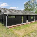Moderne Holzhütte mit Terrasse und Garten. Schwarze Fassade, große Fenster.