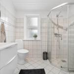 Badezimmer mit Dusche, Toilette und Waschbecken. Fenster und Regal sind sichtbar.