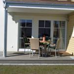 Terrasse mit Tisch, Stühlen und geschlossenem Sonnenschirm. Hintergrund: Fenster und Hauswand.