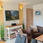 Wohnzimmer mit Fernseher, Sitzgelegenheiten und Tisch. Holztüren und Wandbehang.