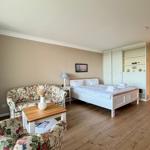 Room with bed, sofa, table, and closet. Wooden floor and beige walls.